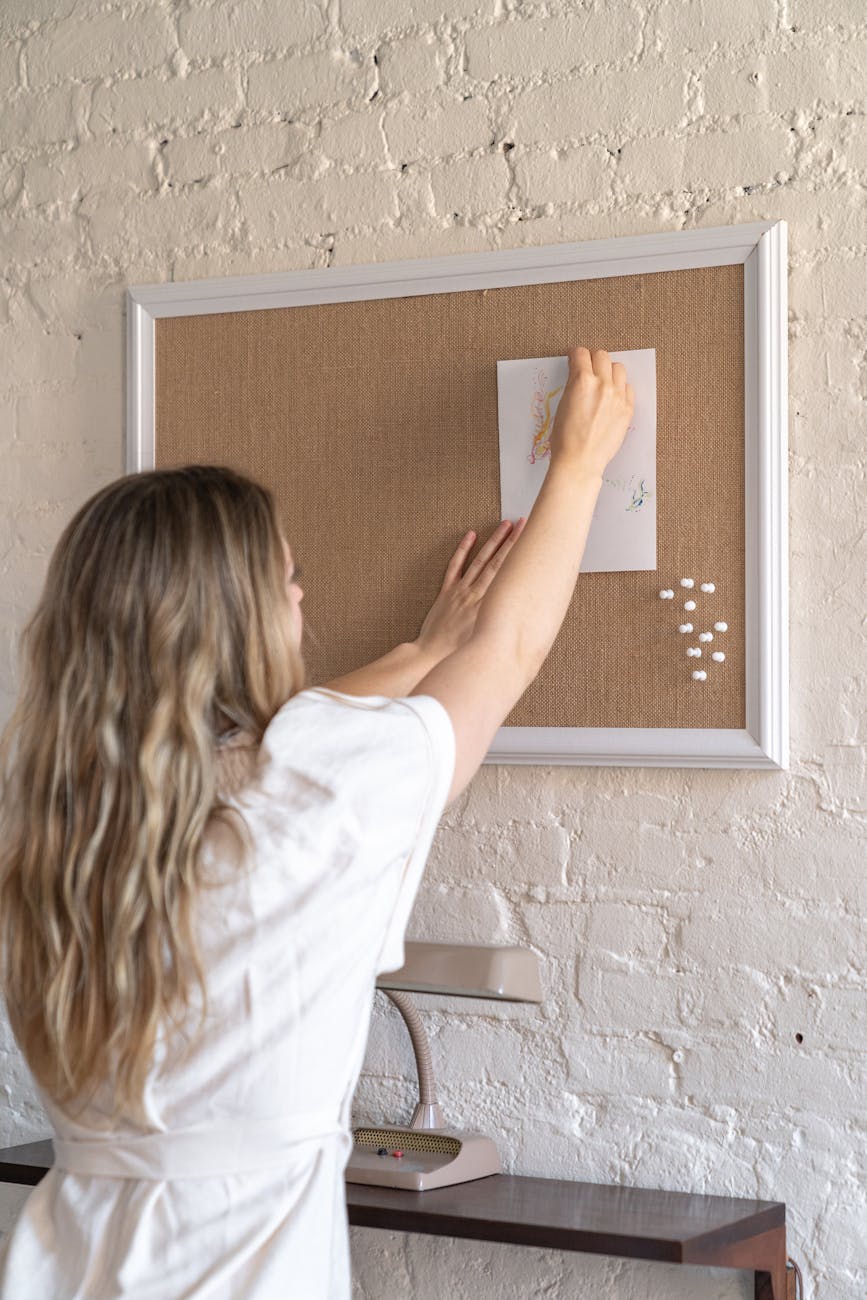 woman in white shirt posting an artwork on a board on the wall